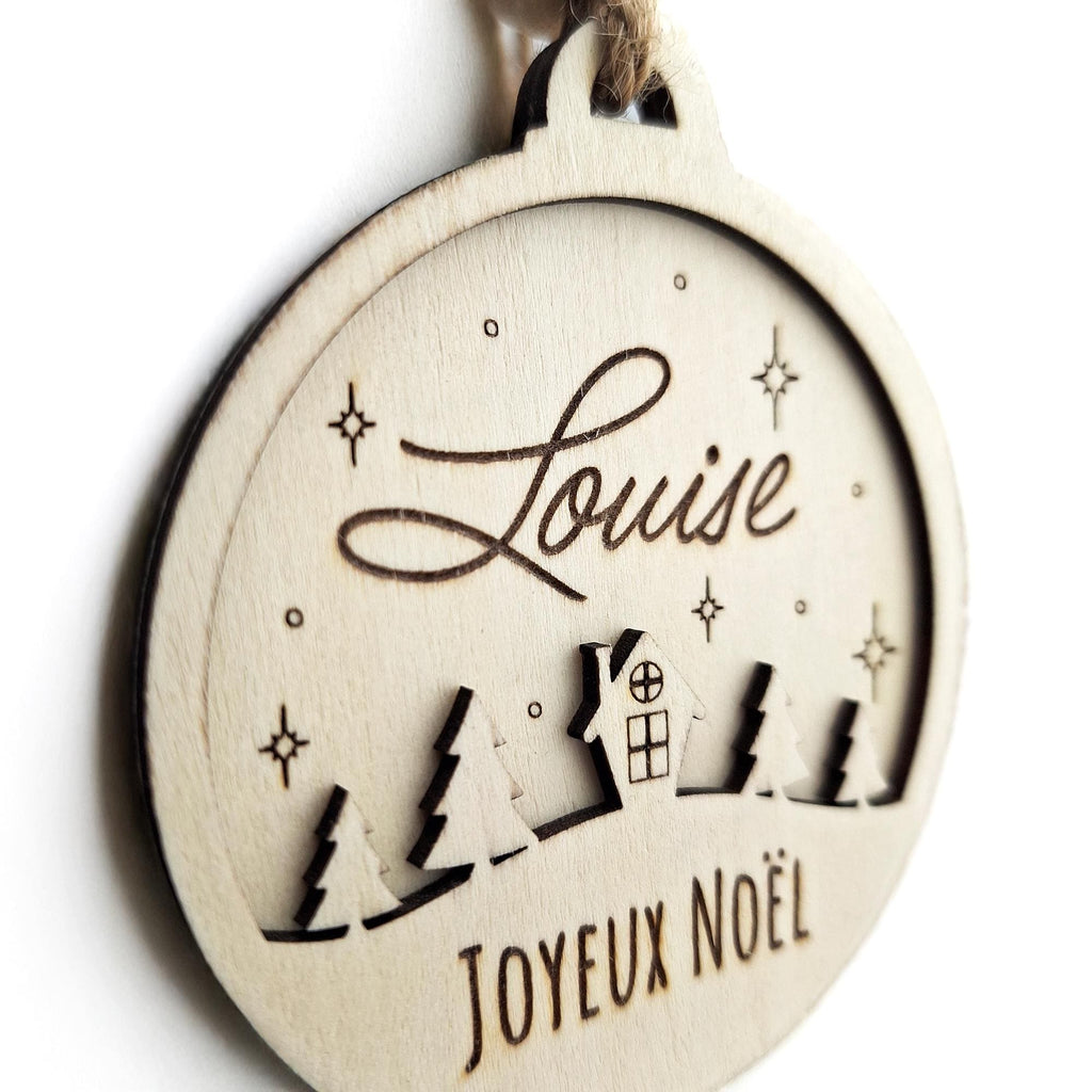 Gros plan sur la boule de Noël en bois Louise avec maisons et sapins découpés
