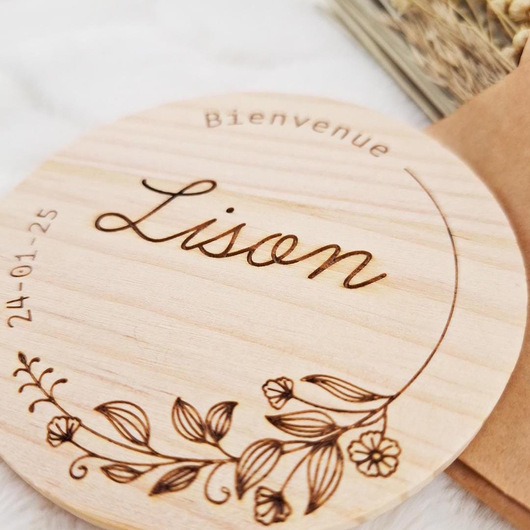 Gros plan sur la carte de naissance en bois « Bienvenue Lison » avec couronne florale